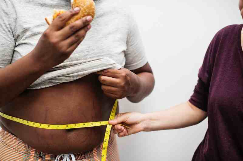 man being measured with a measuring tape while eating a burger